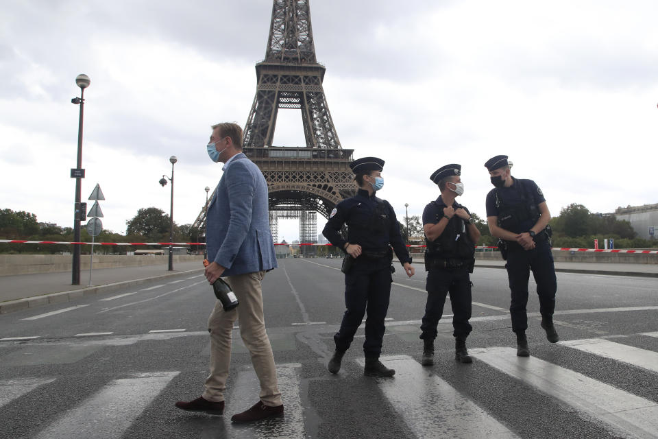 A Russian tourist holding a bottle of Champagne walks past police officers securing the bridge leading to the Eiffel Tower, Wednesday, Sept. 23, 2020 in Paris. Paris police have blockaded the area around the Eiffel Tower after a phone-in bomb threat. (AP Photo/Michel Euler)