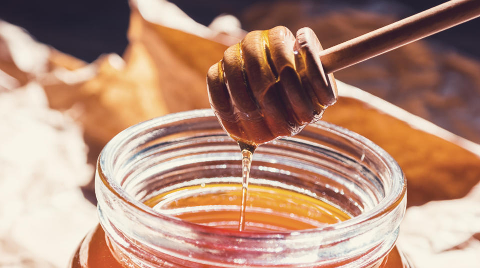 Closeup of a wooden honey dipper that dips in honey in a honey pot. ideal for websites and magazines layouts