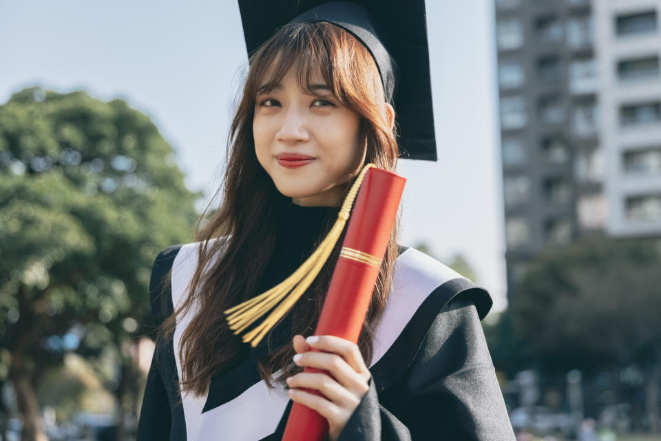 Woman in graduation cap and gown holding a diploma, smiling. Used in a parenting article