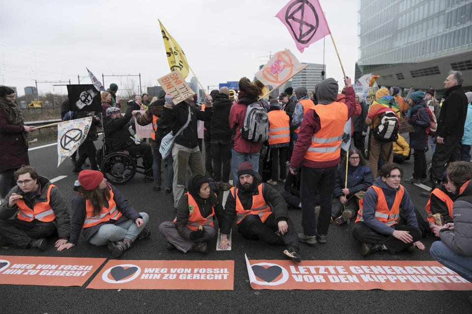 Climate activists glue their hands to the ground while blocking the main highway around Amsterdam near the former headquarters of a ING bank to protest its financing of fossil fuels, Saturday, Dec. 30, 2023. Protestors walked onto the road at midday, snarling traffic around the Dutch capital in the latest road blockade organized by the Dutch branch of Extinction Rebellion. (AP Photo/Patrick Post)