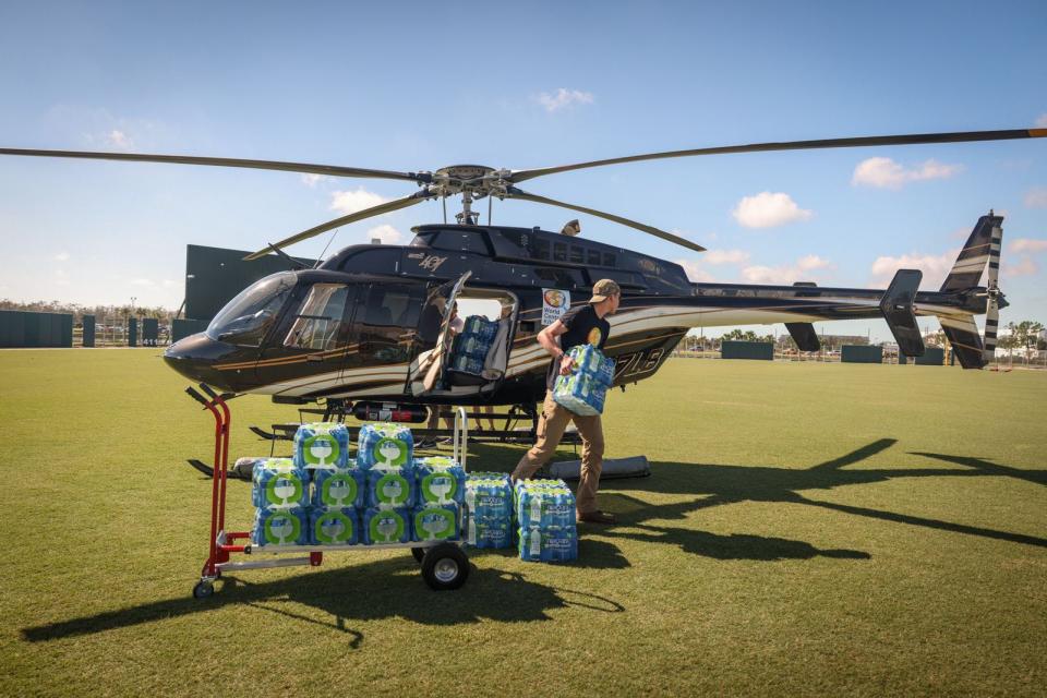 A worker with World Central Kitchen unloads packages of water bottles from a helicopter to help victims of Hurricane Ian.