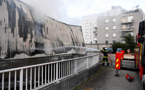 A firefighter sprays water on September 21, 2017 in Grenoble, eastern France, on a burnt-out garage which contained about fifty vehicles of the French gendarmerie, after a fire. - Credit: JEAN-PIERRE CLATOT/AFP