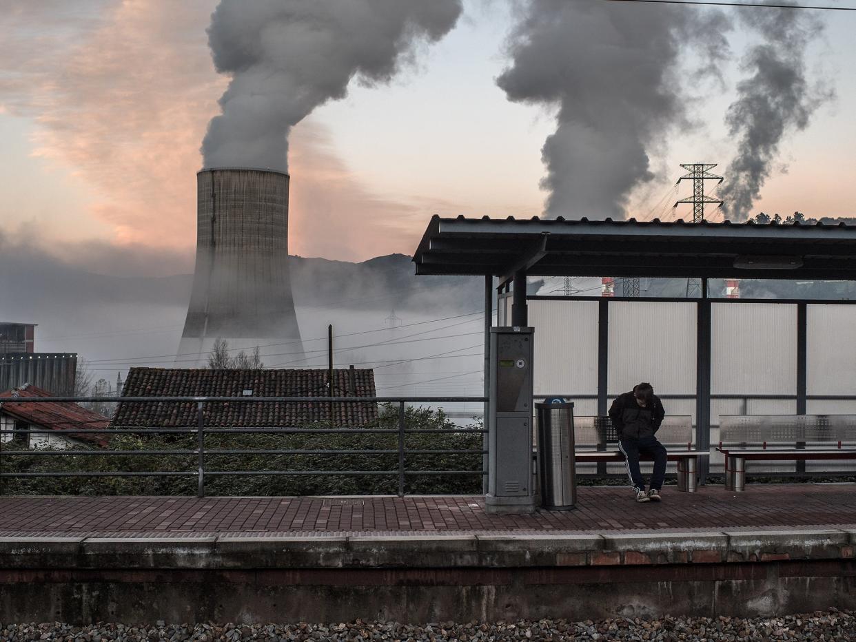A commuter waits for a train at the train station of Las Segadas, in front of the thermal power station of Soto de Ribera in Entrepuentes, Spain: Getty