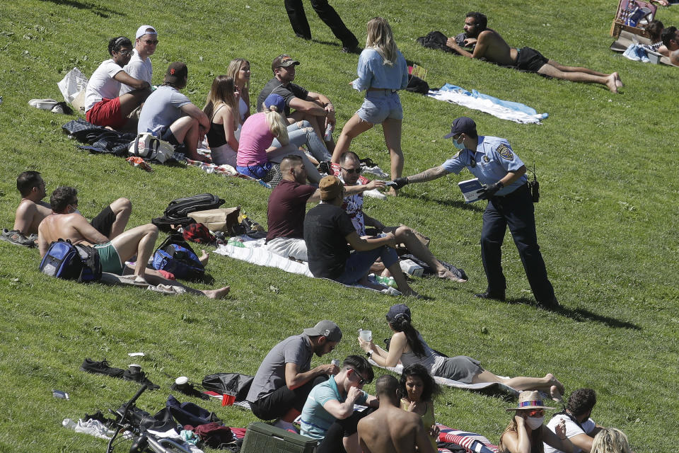 A San Francisco Police cadet hands out face masks to help prevent the spread of the coronavirus, at Dolores Park in San Francisco, Sunday, May 24, 2020. (AP Photo/Jeff Chiu)