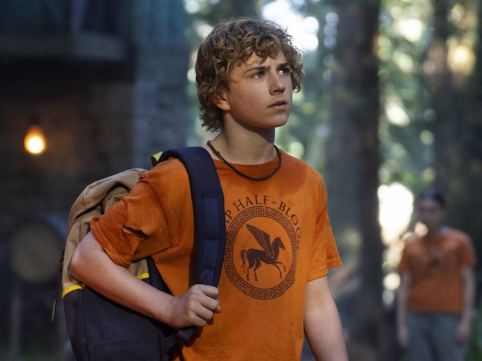 walker scobell as percy jackson in the tv series, wearing an orange camp half-blood shirt and a backpack