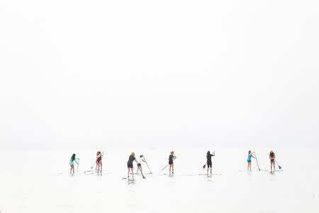 Israeli sap surfers take part in an event for the Jewish holiday of Purim in the Mediterranean sea in Tel Aviv, Israel March 24, 2016. The picture was created by exposing for the shadows on a hazy day. REUTERS/Baz Ratner/Files