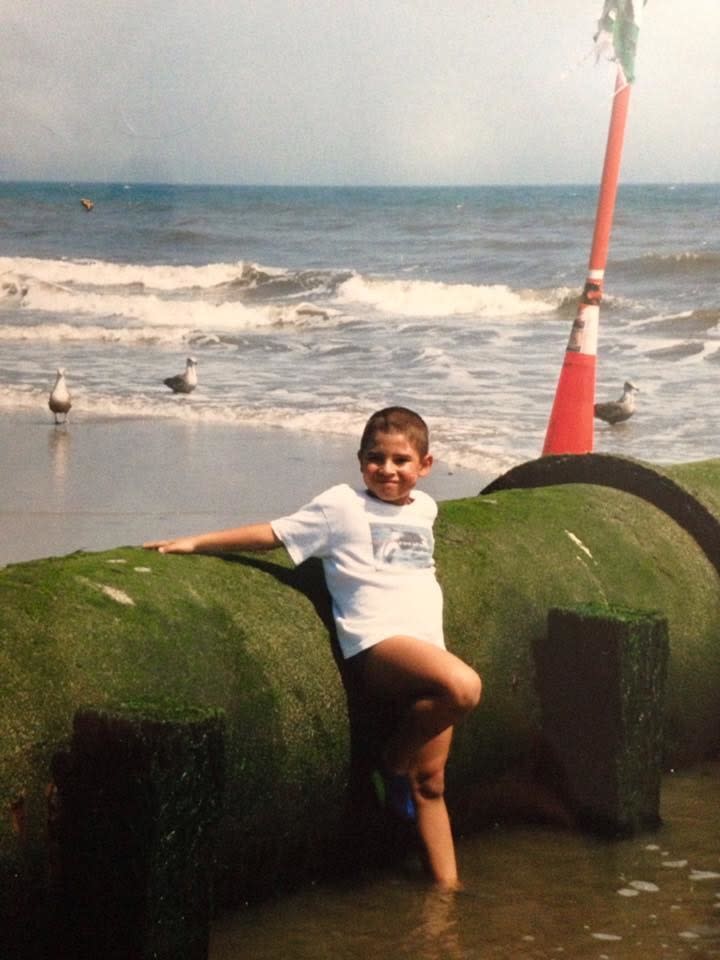 A young child wearing a T-shirt and leaning against a large pipeline by the ocean