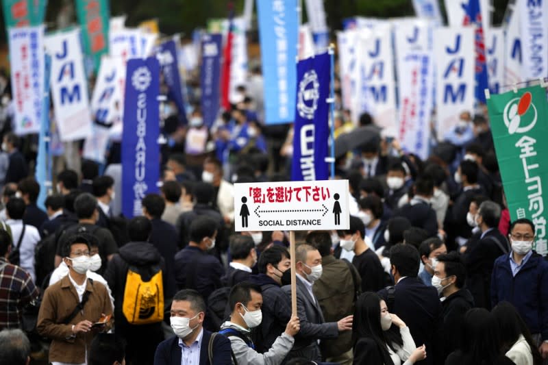 2022年4月29日，東京的防疫工作人員在人群中高舉標語，提醒人們保持社交距離。（美聯社）