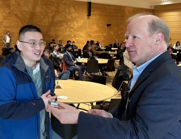 IonQ’s CEO and president, Peter Chapman, shows off a quantum computing chip as Xinxin Tang, a University of Washington researcher studying quantum phenomena, looks on. (GeekWire Photo / Alan Boyle)