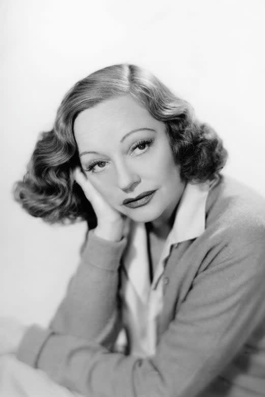 A woman with wavy hair rests her head on her hand, wearing a collared shirt and cardigan. I don't know who she is