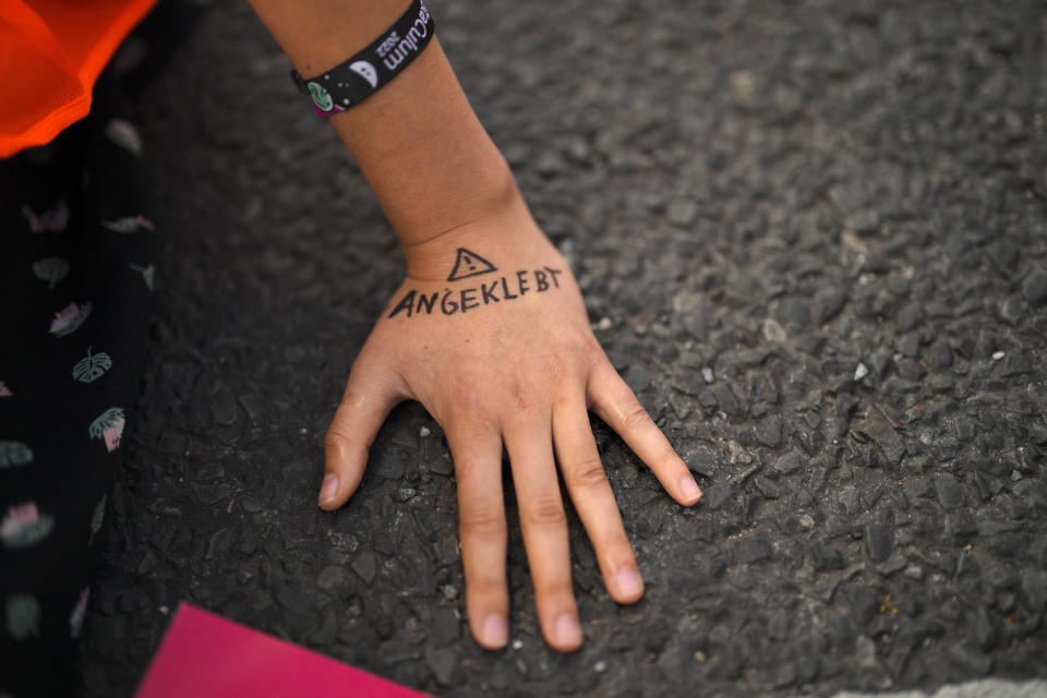 Climate activist Lina Schinkoethe's hand is glued to the ground with a warning to police during a protest with the group Uprising of the Last Generation in Berlin, Germany, Tuesday, June 21, 2022. The group claims the world has only a few years left to turn the wheel around and avoid catastrophic levels of global warming. (AP Photo/Markus Schreiber)