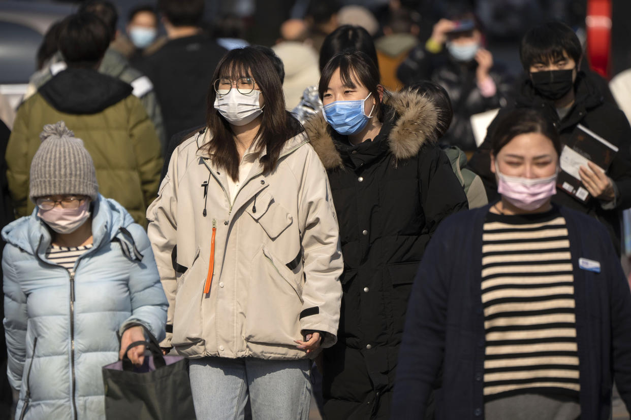 People wearing face masks walk across an intersection in Beijing, Tuesday, Feb. 7, 2023. (Mark Schiefelbein / AP)