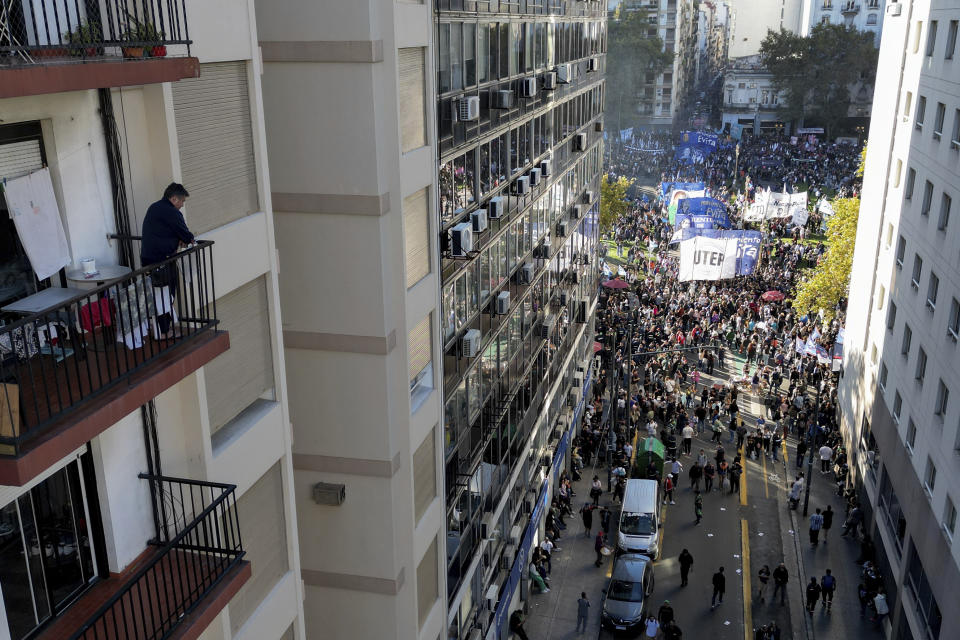 A resident watches demonstrators march to demand more funding for public universities and protest against austerity measures proposed by President Javier Milei in Buenos Aires, Argentina, Tuesday, April 23, 2024. (AP Photo/Rodrigo Abd)