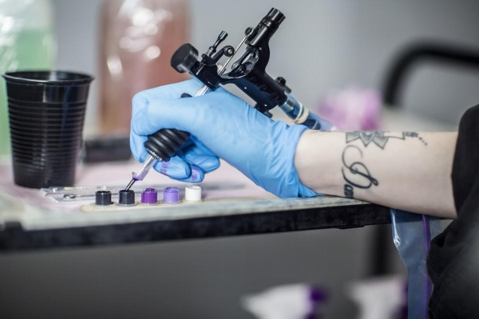 tattoo artist dipping gun into ink