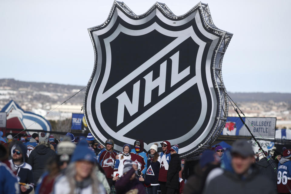 FILE - In this Saturday, Feb. 15, 2020, file photo, fans pose below the NHL league logo at a display outside Falcon Stadium before an NHL Stadium Series outdoor hockey game between the Los Angeles Kings and Colorado Avalanche, at Air Force Academy, Colo. The NHL nailed down the final details of a playoff format if the season can resume on the same day word came out that another player has tested positive for the coronavirus. (AP Photo/David Zalubowski, File)