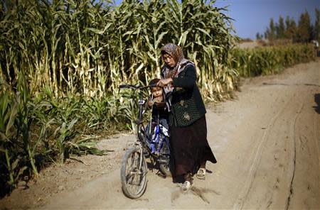 An ethnic Uighur woman pushes a bicycle with her son on it along a dirt road in Turpan, Xinjiang province in this October 31, 2013 file photo. REUTERS/Carlos Barria/Files