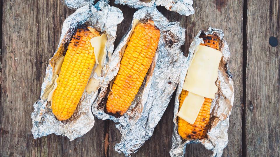 Three corn on the cobs grilled in foil with butter and cheese
