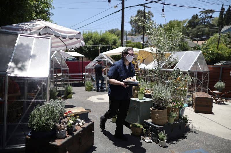 A waiter carries plates past social distancing greenhouse dining pods in the former parking lot of the Lady Byrd Cafe in Los Angeles