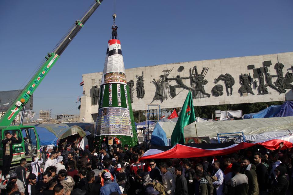 Demonstrators work to install a Christmas tree, with posters of protesters who have been killed in demonstrations and their belongings, while anti-government protesters hold a national flag during a sit-in at Tahrir Square in Baghdad, Iraq, Tuesday, Dec. 24, 2019. (AP Photo/Khalid Mohammed)