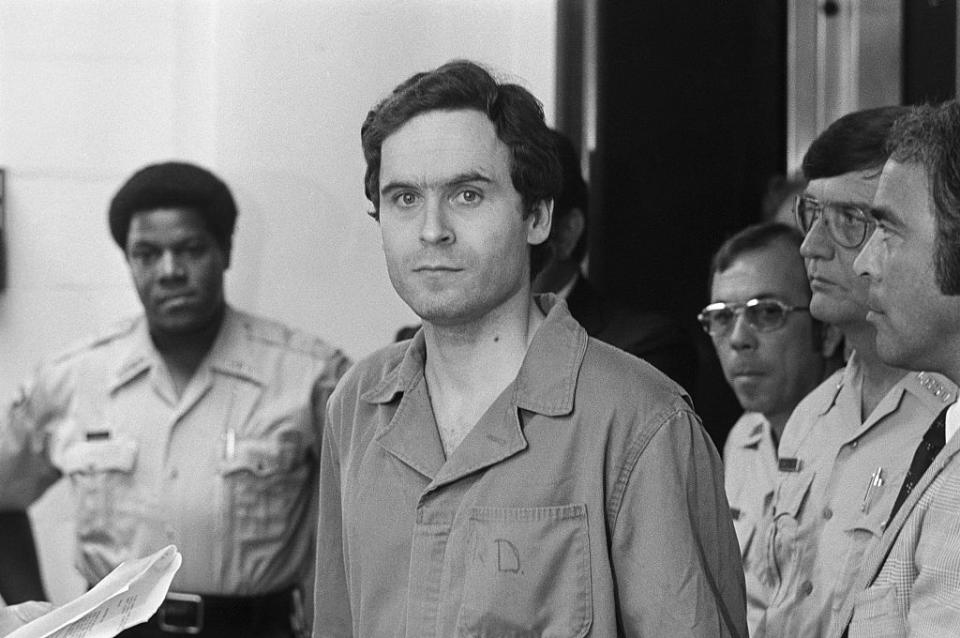 ted bundy surrounded by police and looking straight ahead as he walks into a court hearing