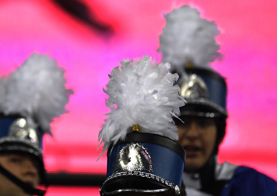 The Wyoming High School Marching band sits ready as a cold wind ruffles their feathers with a neon background at the OHSAA State Football Division IV Championship at Tom Benson Hall of Fame Stadium in Canton.