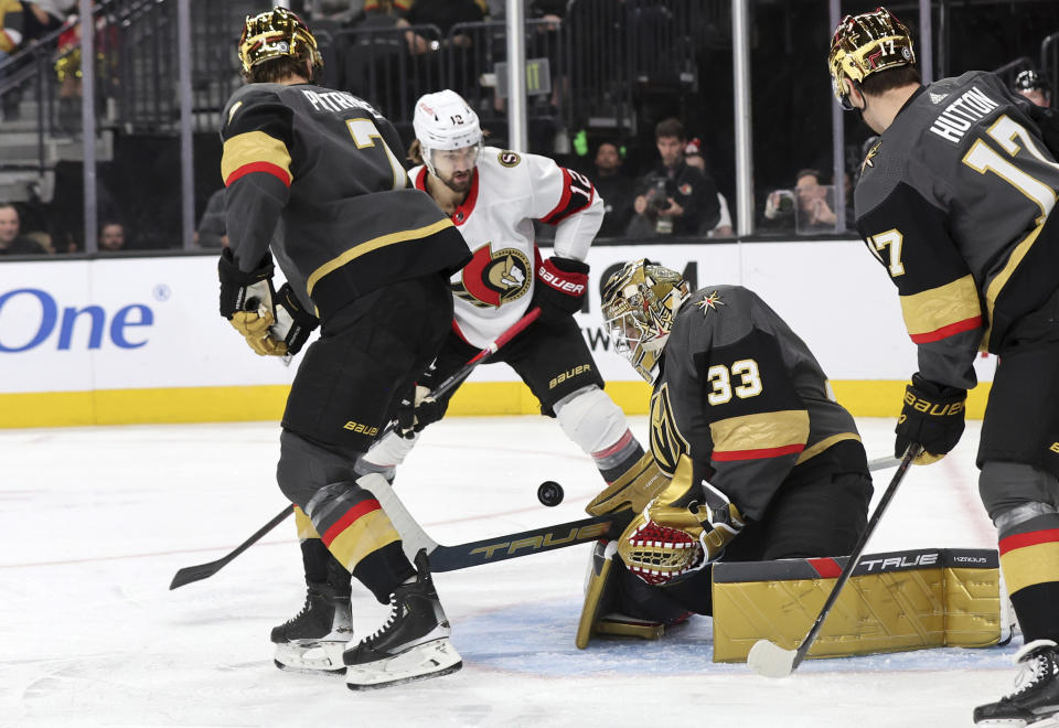 Vegas Golden Knights goaltender Adin Hill (33) blocks a shot by Ottawa Senators center Mark Kastelic (12) during the first period of an NHL hockey game, Sunday, Dec. 17, 2023, in Las Vegas. Also defending are Vegas Golden Knights defenseman Alex Pietrangelo, left, and defenseman Ben Hutton (17). (AP Photo/Steve Marcus)