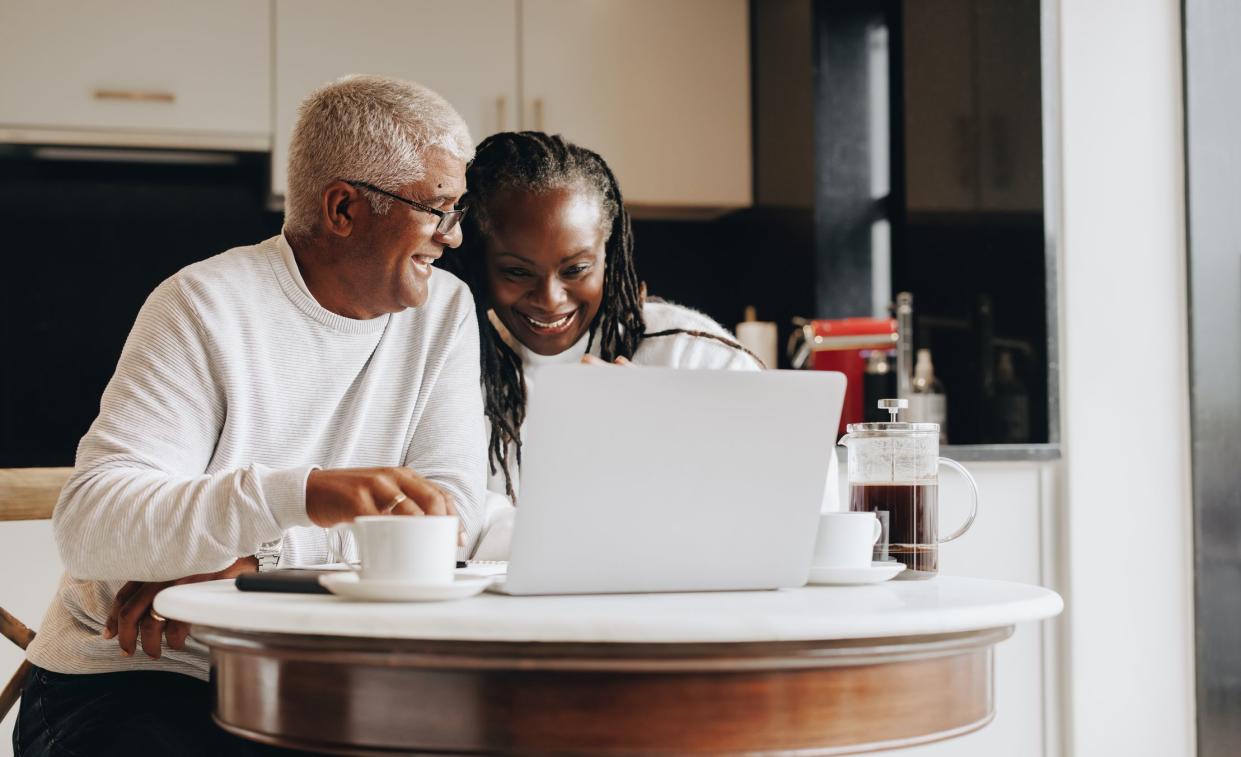 Happy senior couple having a video call on a laptop at home. Mature couple having a virtual meeting with a retirement consultant. Ethnic senior couple planning their retirement together.