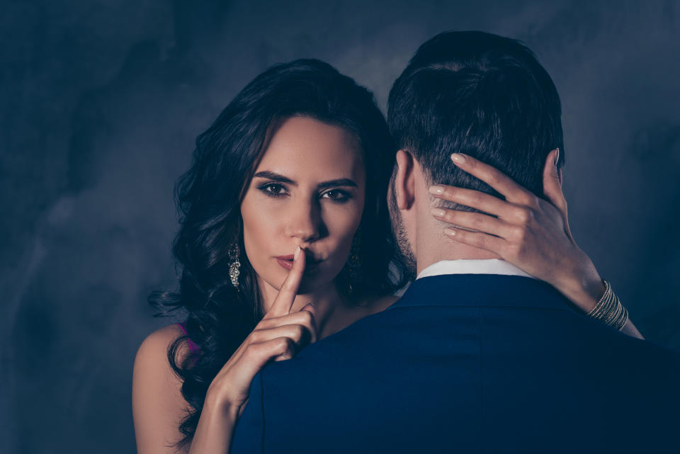 Shh! Portrait of tempting brunette lady showing silence sign with forefinger touching secret mysterious gentlemen with rear view, lovely Mr and Mrs isolated on grey background