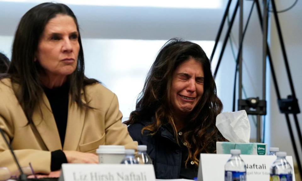 Two white women with long dark hair sit next to each other. The one on the left looks serious, while the one on the right cries.