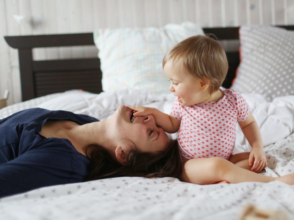 A mom playing with her baby girl on a bed