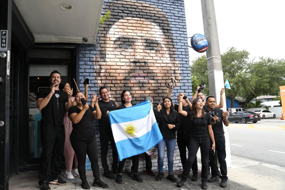 Staff at the Fiorito restaurant hold an Argentinian flag as they pose for a photograph in front of a Messi mural. (AP Photo/Lynne Sladky)