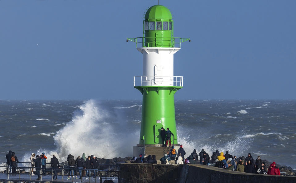 People stand near the lighthouse on the pier of Warnemunde in stormy weather in Rostock, Germany on Sunday Jan. 30, 2022. (Jens Buttner/dpa via AP)