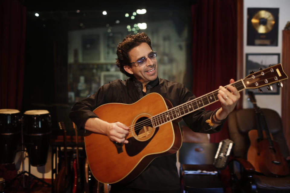 En esta foto del 25 de noviembre del 2019, el compositor y productor George Noriega toca la guitarra de su infancia en su estudio en Davie, Florida. Noriega ha producido éxitos de la música latina como "Calma" de Pedro Capó, ganadora del Latin Grammy a la canción del año en noviembre. (AP Foto/Brynn Anderson)