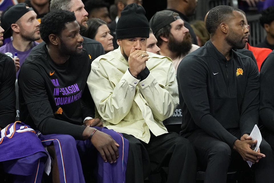 Phoenix Suns guard Devin Booker warms his hands on the bench during the first half of an NBA basketball game against the Los Angeles Lakers , Friday, Nov. 10, 2023, in Phoenix. (AP Photo/Matt York)