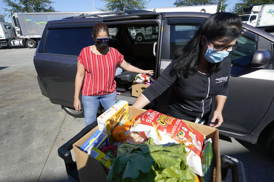 Johnna Nieves, left, opens her van as Idalia Nunez, right, of the Second Harvest Food Bank loads the vehicle with a weeks supply of food in Orlando, Fla., on Tuesday, Nov. 17, 2020. While food banks have become critical during the pandemic, they’re just one path for combating hunger. For every meal from a food bank, a federal program called Supplemental Nutrition Assistance Program, or food stamps _ provides nine. (AP Photo/John Raoux)
