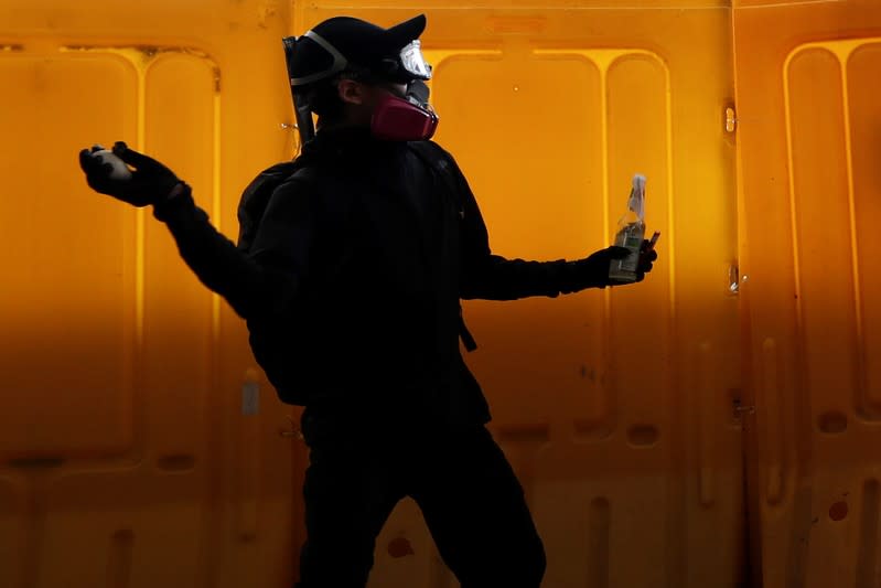 A protester throws a stone while holding a Molotov cocktail from behind a barricade during clashes with riot police at Hong Kong Polytechnic University in Hong Kong