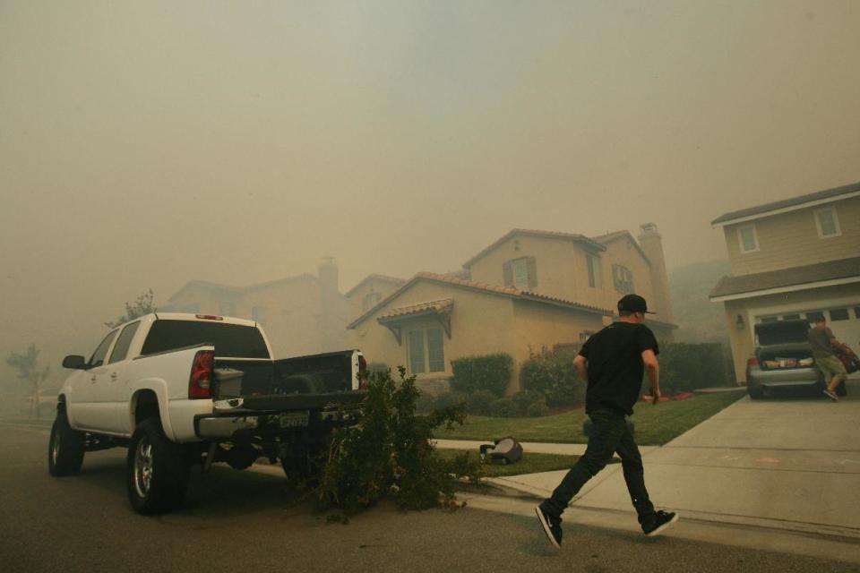 A resident rushes to help evacuate a home as a brush fire burning in Day Creek near the Etiwanda Preserve in Rancho Cucamonga, Calif., nears their neighborhood on Wednesday, April 30, 2014. Fire officials say winds gusting to 60 mph are pushing the flames through the foothills of the San Bernardino Mountains east of Los Angeles, although no homes are in immediate danger. Several neighborhoods and at least seven schools in Rancho Cucamonga have been evacuated. There’s no word on what sparked the blaze but it comes in the midst of a heat wave that’s created extreme fire danger. (AP Photo/The Press-Enterprise, Stan Lim) MAGS OUT; MANDATORY CREDIT