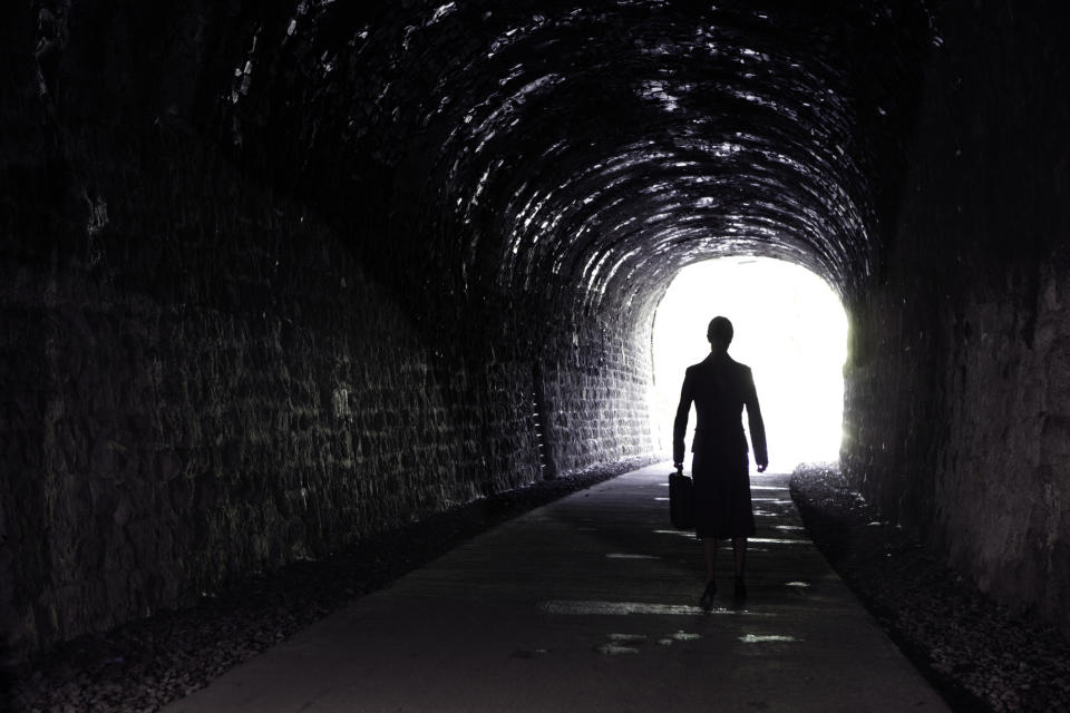 A silhouette is walking through a dark tunnel