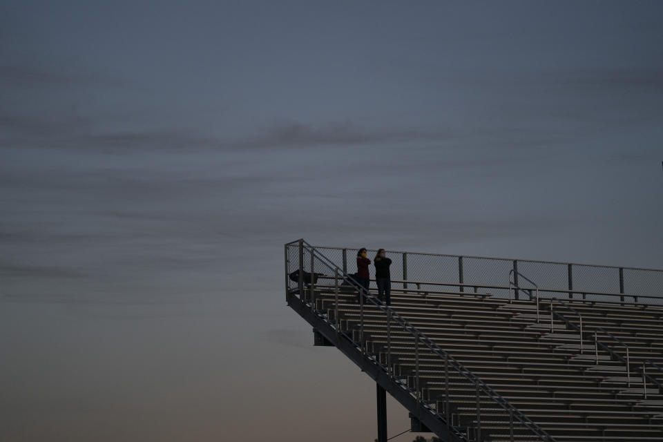 Dusk settles as two spectators watch a high school football game between El Modena and El Dorado in Orange, Calif., Friday, March 19, 2021. (AP Photo/Jae C. Hong)