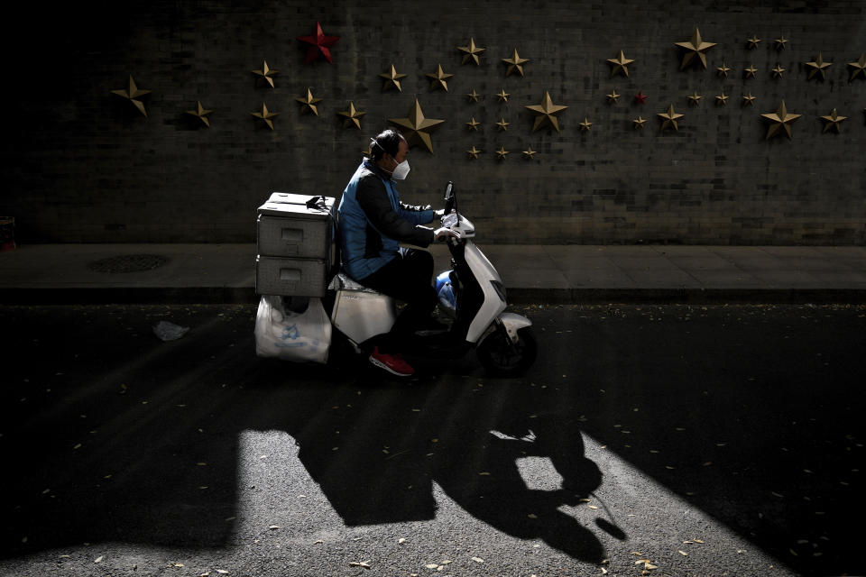 A food delivery rider wearing a face mask rides past communist symbol of stars on display outside a restaurant in Beijing, Monday, Oct. 31, 2022. (AP Photo/Andy Wong)