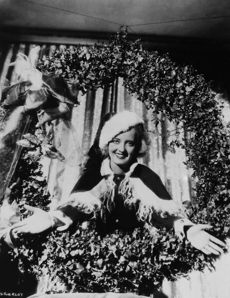 <p>Bette Davis wears a fur-trimmed cape and cap, just like Mrs. Claus herself, as she poses inside a giant wreath during holidays.</p>