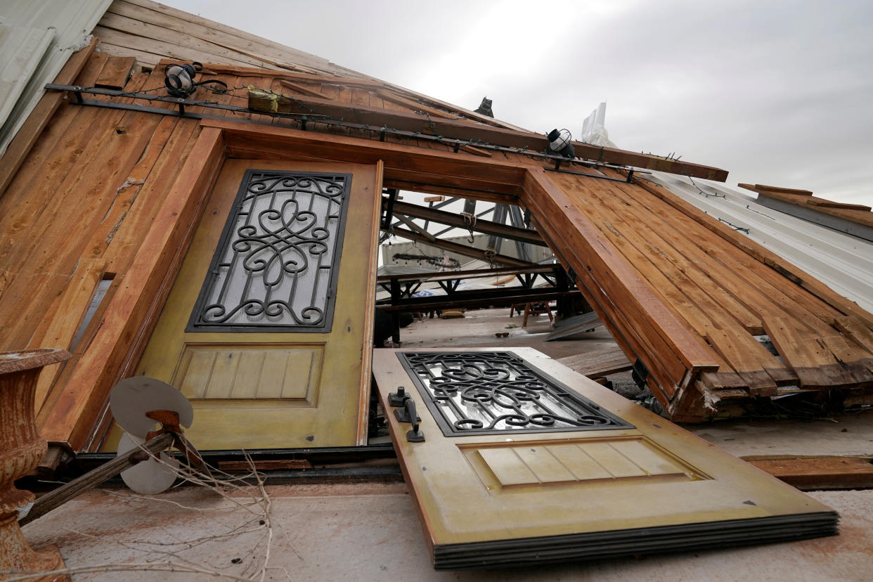 A front door with intricate grillwork lies on the ground, torn from its hinges.