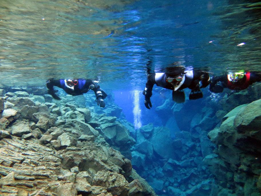 This Jan. 23, 2013 photo provided by the diving excursion company DIVE.IS shows snorkelers traversing Iceland’s Silfra, a rift fed by glacier water. Because of its pure water and stunning colors, Silfra has become a popular site for divers despite near-freezing temperatures. (AP Photo/DIVE.IS, Louis Kotze)