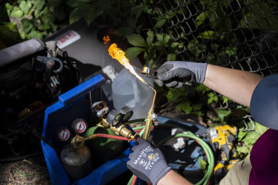 Jennifer Byrne, owner and technician at Comfy Heating and Cooling, prepares a torch to repair an air conditioning condenser unit in Philadelphia on Thursday, Sept. 14, 2023. Refrigerants are chemical fluids that have made air conditioning and refrigeration possible, but they are hundreds or even thousands of times more powerful at warming the planet than carbon dioxide, the most notorious greenhouse gas. (AP Photo/Joe Lamberti)