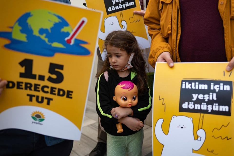 A young girl holding a babydoll stands between placards during a protest rally as part of a global day of action on climate change in Istanbul, on November 6, 2021 (AFP via Getty Images)