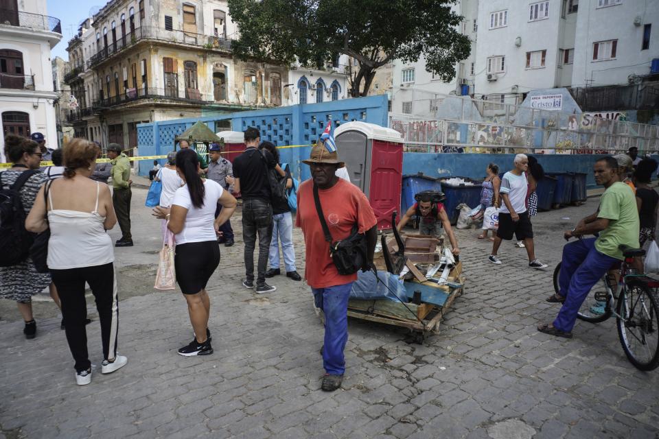 People transport a crate of used furniture past Villegas street which is cordoned off with caution tape due to a building, left, that partially collapsed the previous week, killing three people, in Havana, Cuba, Thursday, Oct. 5, 2023. The Cuban government has acknowledged the problem of housing deterioration in the island, but says the lack of material resources prevents it from tackling it. (AP Photo/Ramon Espinosa)
