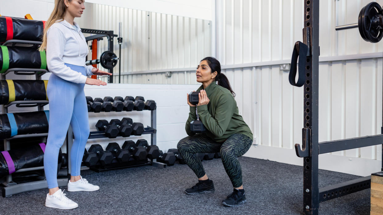  A coach teaching a client how to squat with a dumbbell. 