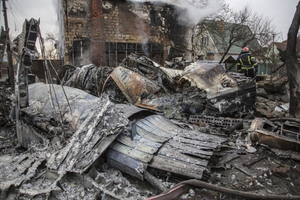 A Ukrainian firefighter, right, walks around wreckage of a downed aircraft in Kyiv, Ukraine.