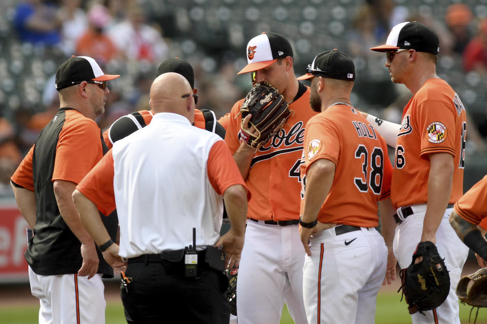 Baltimore Orioles starting pitcher John Means, center, speaks to a trainer before leaving the game with an apparent injury in the first inning of a baseball game against the Cleveland Indians, Saturday, June 5, 2021, in Baltimore. (AP Photo/Will Newton)