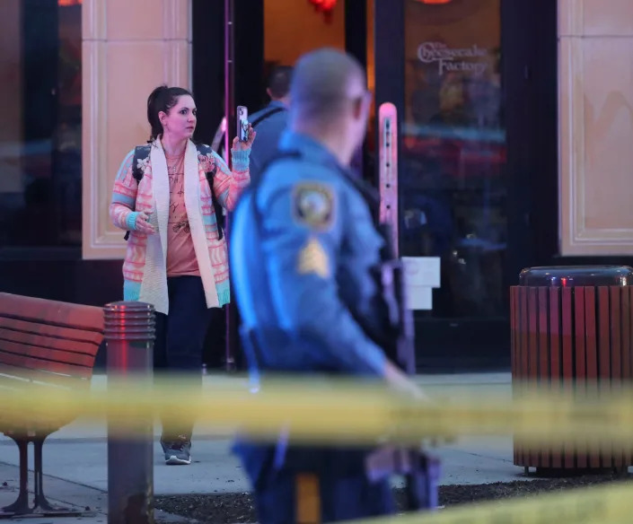 A woman records the scene as she is allowed to leave the Cheesecake Factory restaurant as police, fire and medical personnel respond in force to the food court entrance at the Christiana Mall after a shooting Saturday evening, April 8, 2023.